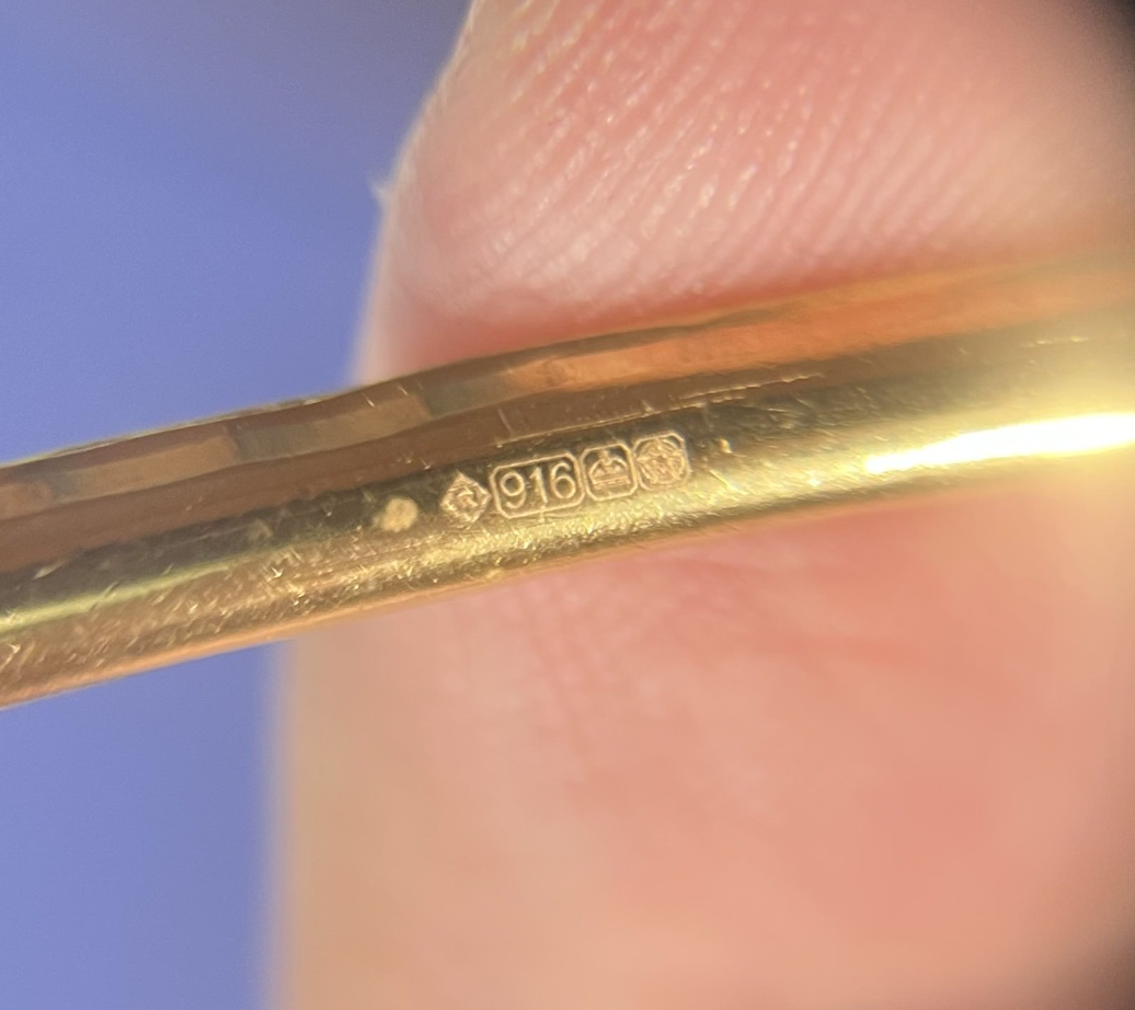 A 916 hallmark on a gold band, seen close up through a jeweller’s loupe.