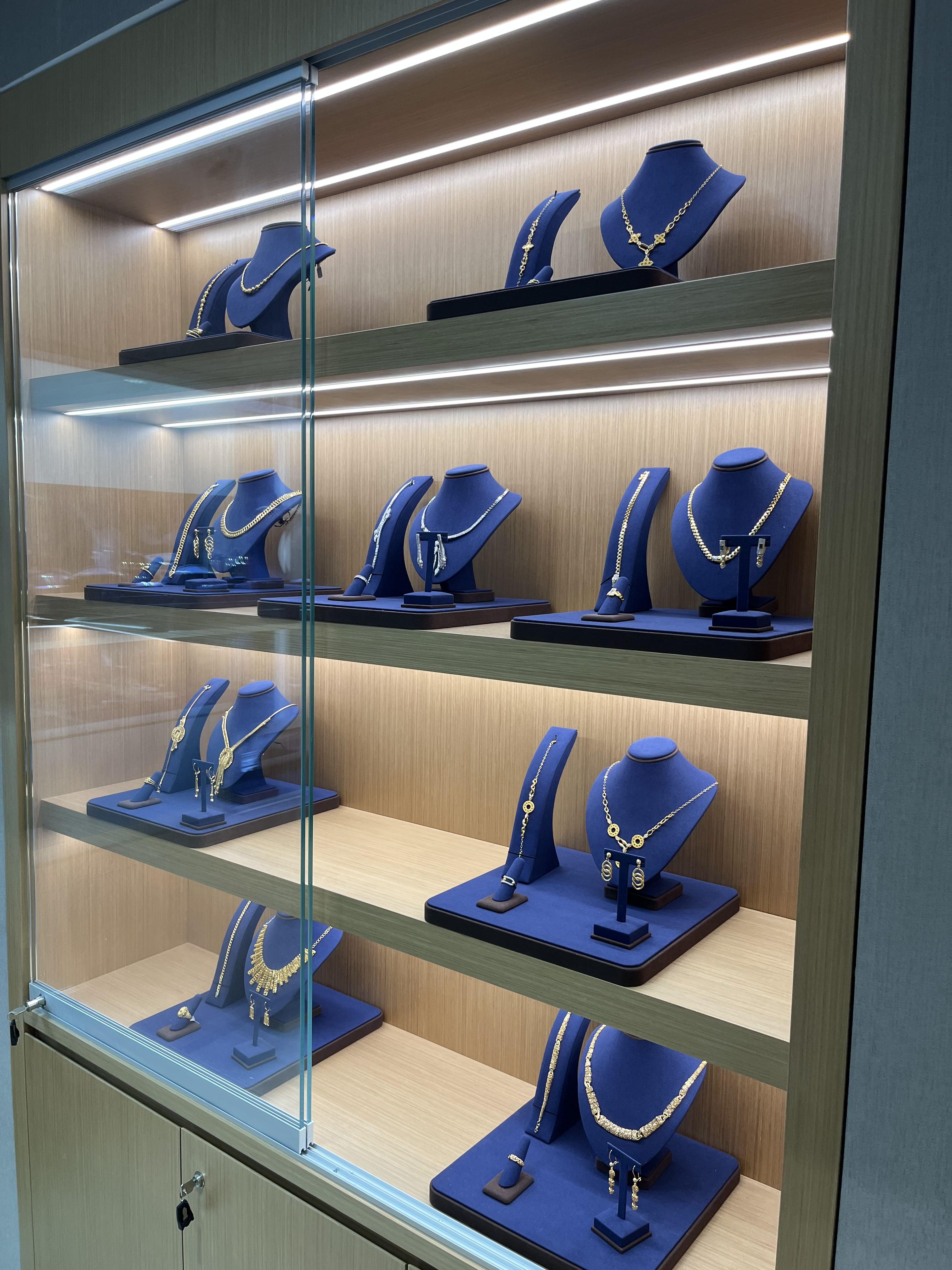 Gold necklaces, bracelets and earrings on navy stands in a lit display cabinet.