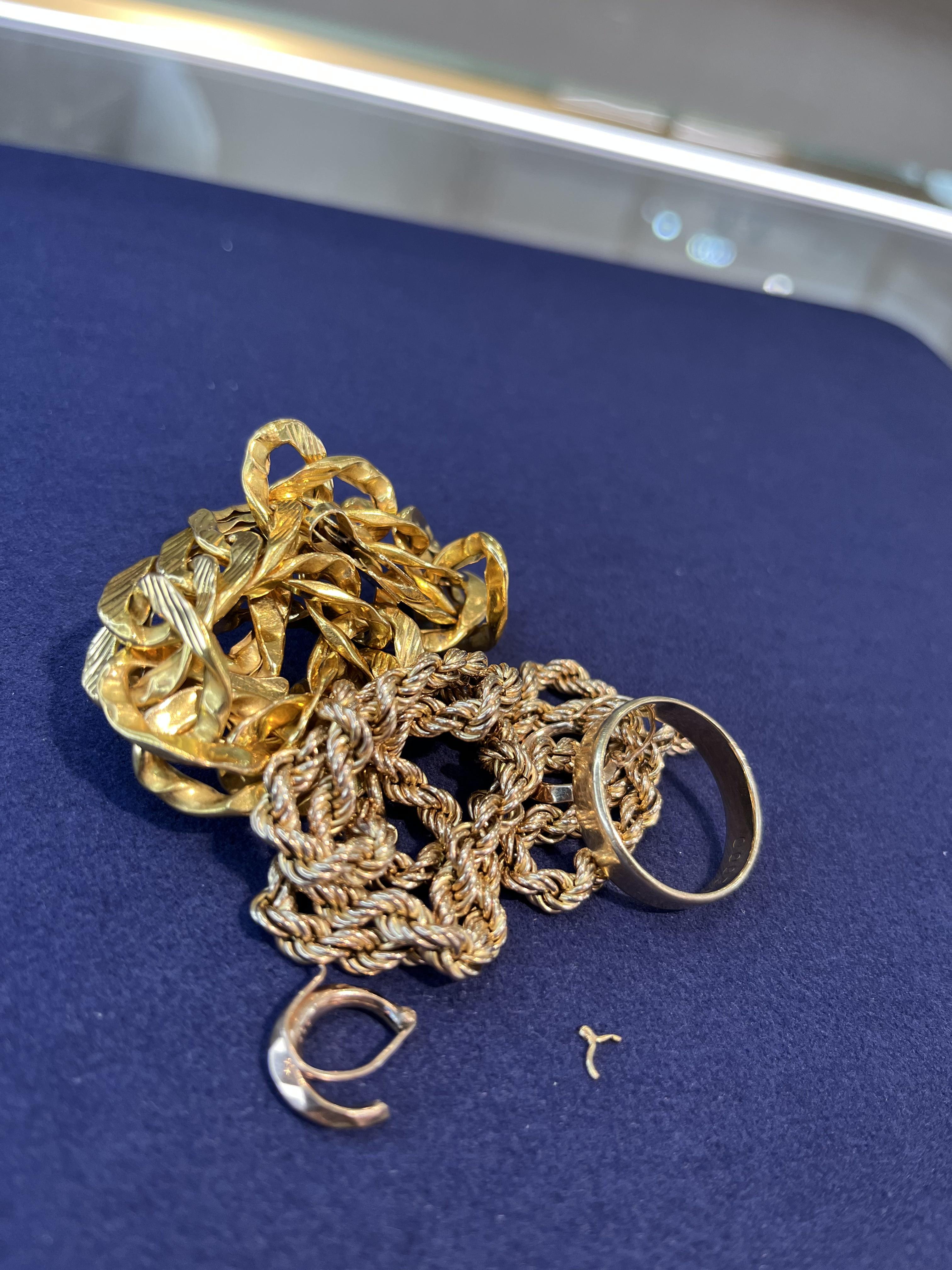 A tangle of gold chains, a worn wedding band and a broken earring on navy velvet at the counter.