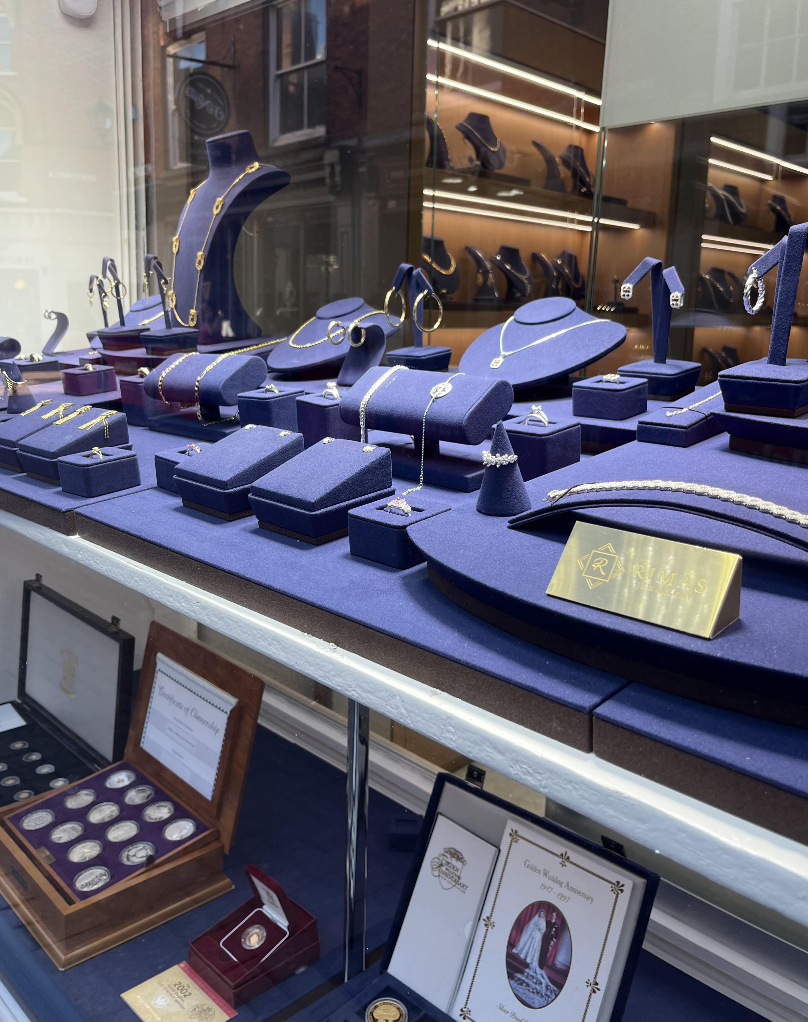 The shop window: gold and silver necklaces, rings and earrings on navy stands, with boxed coin sets below.