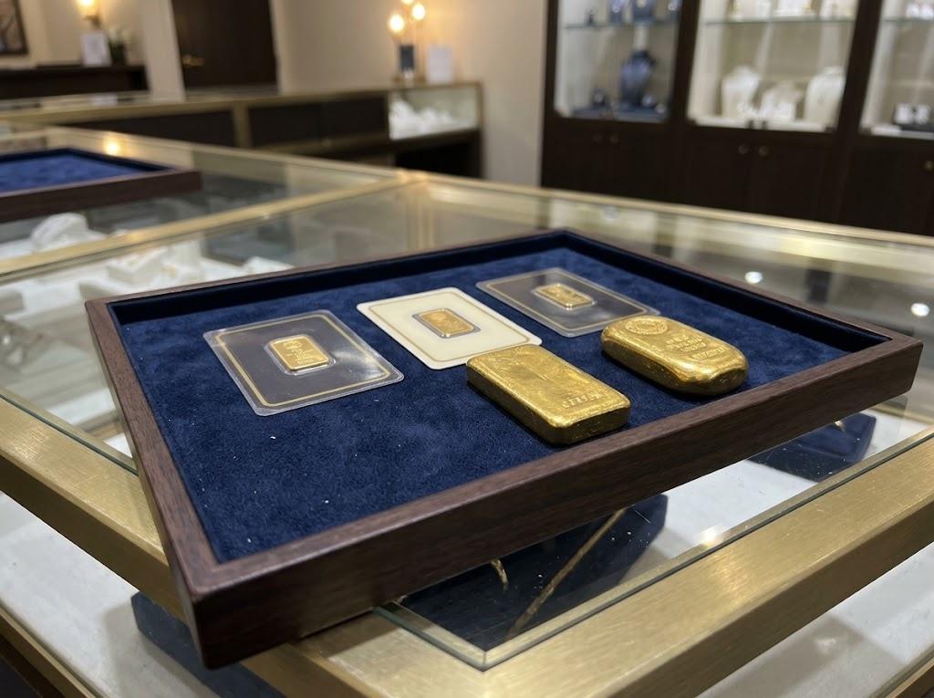 Small gold bars in their certificate cards beside two larger cast gold bars, on a navy velvet tray on the counter.