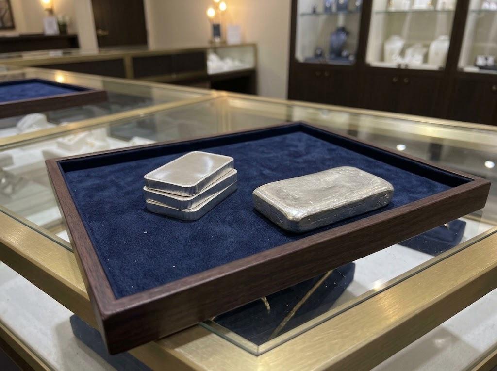 A short stack of minted silver bars beside a larger cast silver bar, on a navy velvet tray on the counter.