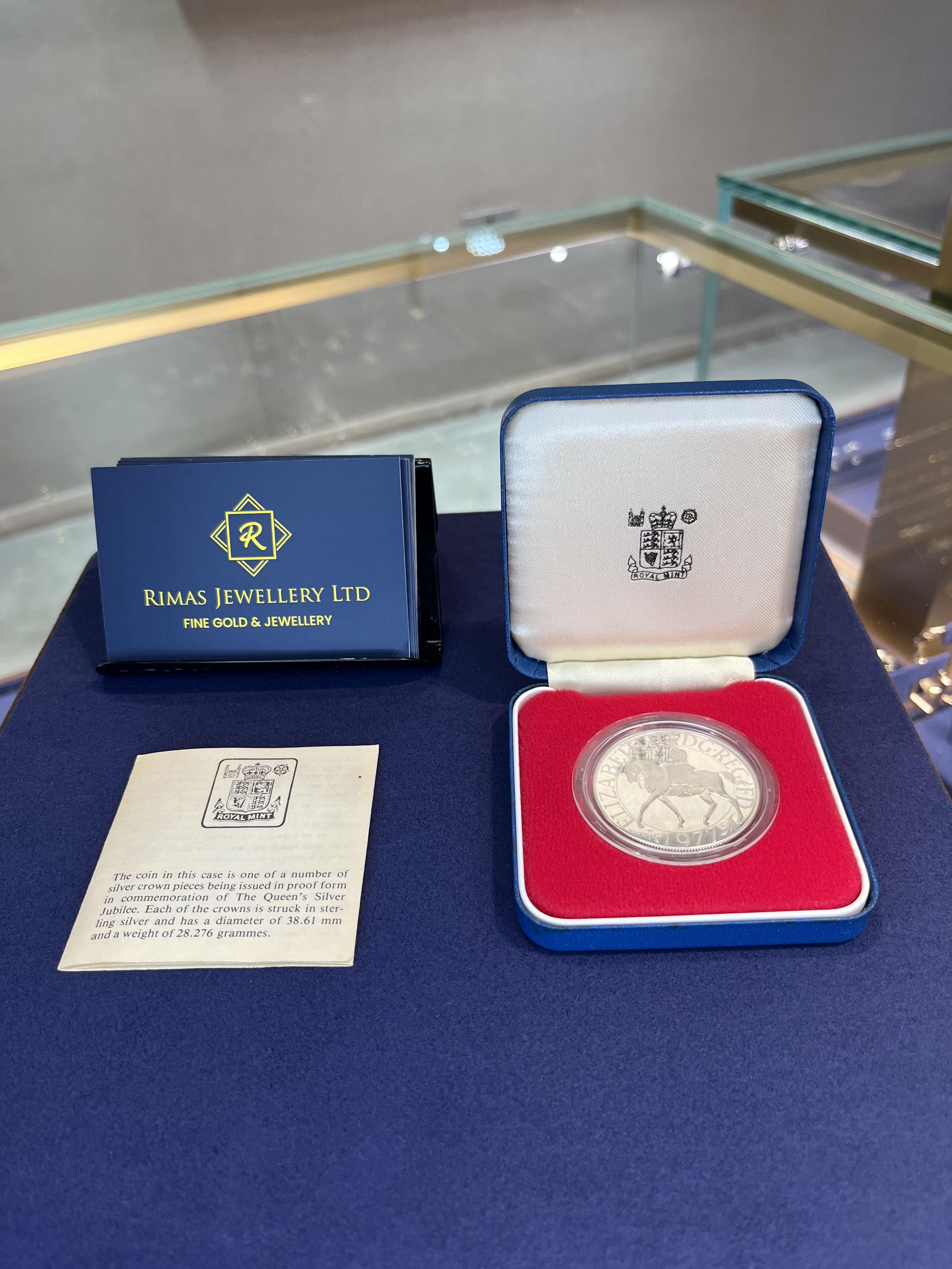 A 1977 Silver Jubilee proof crown in its Royal Mint case, beside its leaflet and a Rimas Jewellery card.